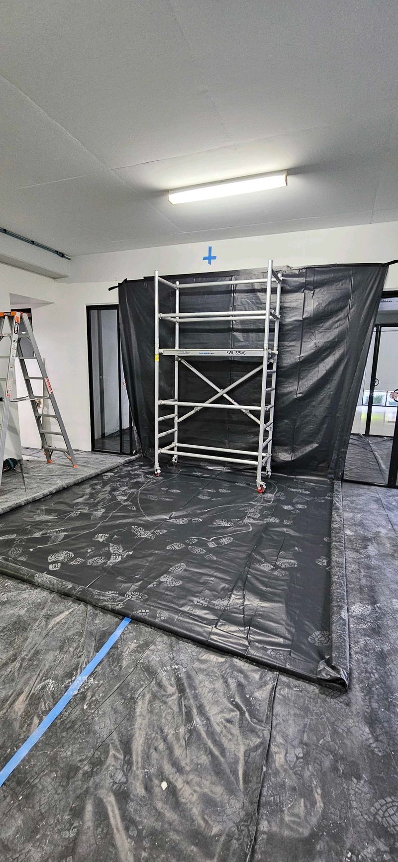 Indoor construction setup with ladders and protective floor covering