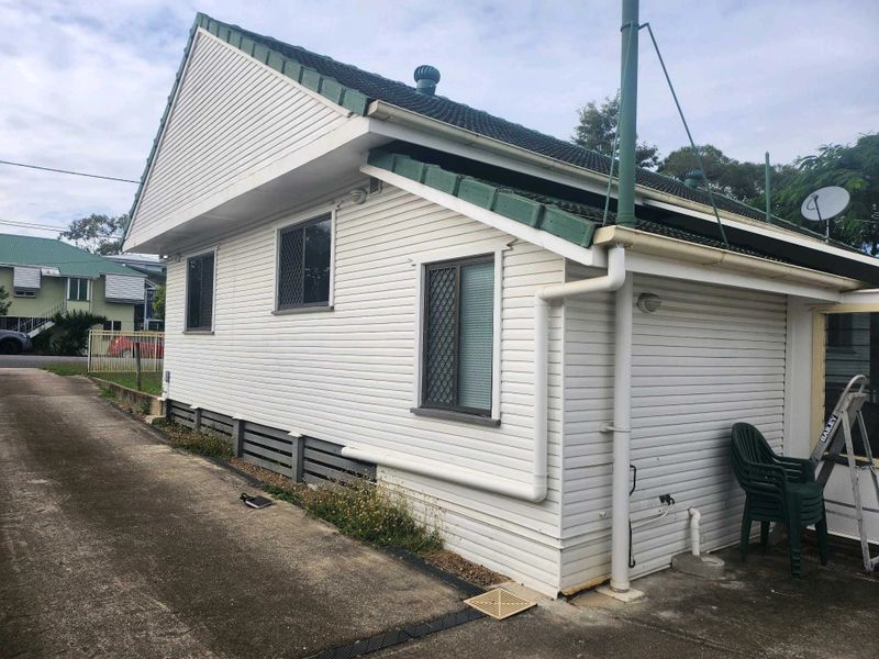 Small white house with green roof and driveway beside it
