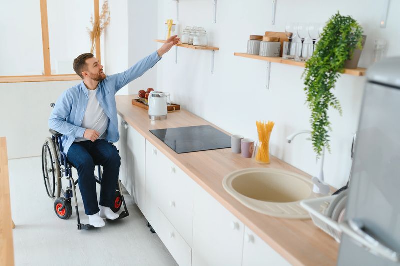 Man in wheelchair reaching for an item on a high kitchen shelf